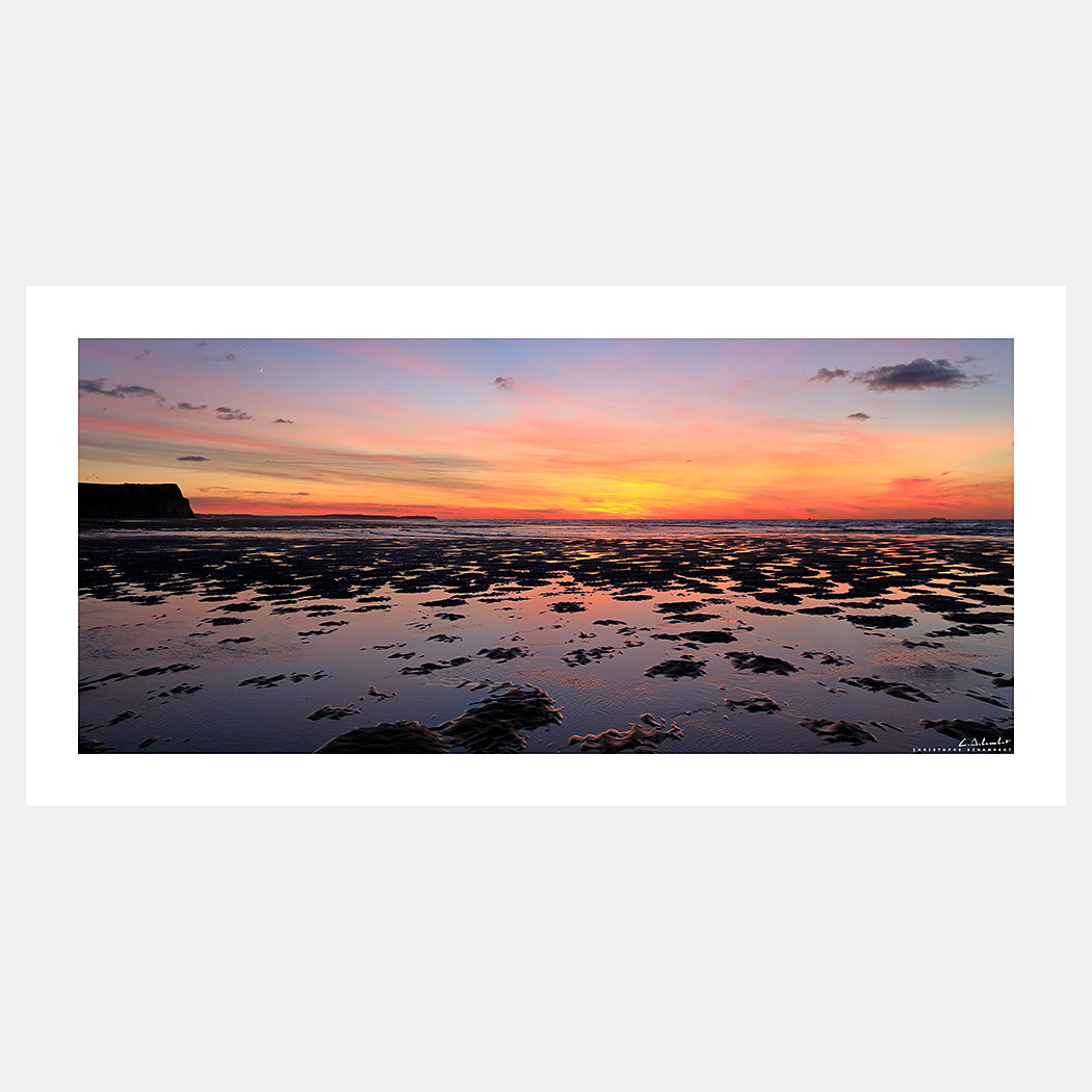 Photographie panoramique d'un coucher de soleil orangé sur la baie de Wissant à marée basse avec le Cap Gris-Nez au loin, Côte d'Opale, Pas-de-Calais, Hauts-de-France, France.