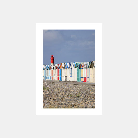 Photographie des cabines de bain multicolores de Cayeux-sur-Mer depuis la plage de galets et avec le phare de Brighton en arrière-plan, en cadrage vertical, Côte Picarde, Somme, Hauts-de-France, France. Design sans légende.