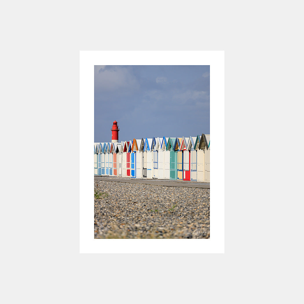 Photographie des cabines de bain multicolores de Cayeux-sur-Mer depuis la plage de galets et avec le phare de Brighton en arrière-plan, en cadrage vertical, Côte Picarde, Somme, Hauts-de-France, France. Design sans légende.
