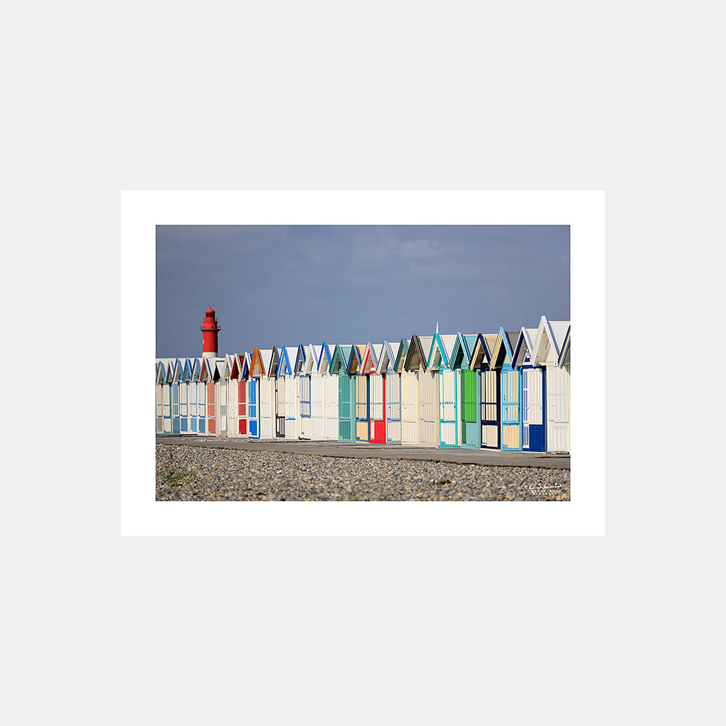 Photographie des cabines de bain multicolores de Cayeux-sur-Mer depuis la plage de galets et avec le phare de Brighton en arrière-plan, en cadrage horizontal, Côte Picarde, Somme, Hauts-de-France, France. Design sans légende.
